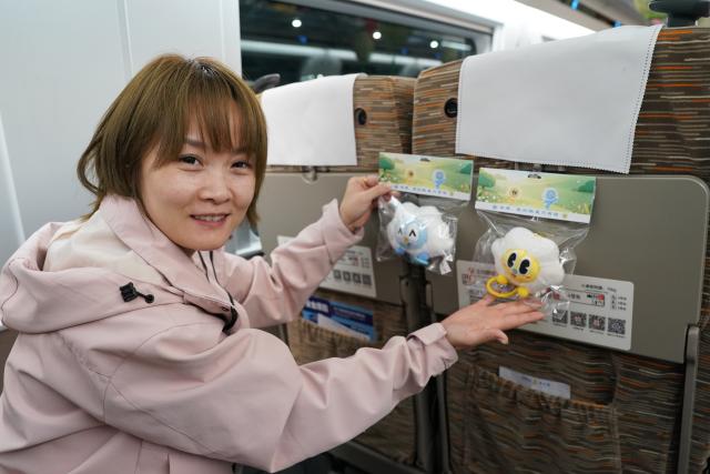 (260928) -- XI'AN, Sept. 28, 2026 (Xinhua) -- A passenger demonstrates cultural and creative products on G9997, the first train of the Xi'an-Ankang high-speed railway, in northwest China's Shaanxi Province, Sept. 28, 2026. The Xi'an-Ankang high-speed railway was officially put into operation on Monday, cutting the railway travel time between Xi'an and Ankang to less than one hour. Spanning about 171 kilometers and with a design speed of 350 kilometers per hour, the railway runs through the cities of Xi'an, Shangluo and Ankang in Shaanxi Province and has five stations along the line. (Xinhua/Shao Rui)