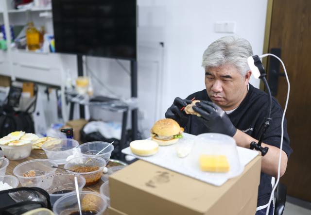 (260929) -- SHANGHAI, Sept. 29, 2026 (Xinhua) -- Li Haohan works on a hamburger at his studio in Shanghai, east China, Sept. 24, 2026. Unlike chefs who prioritize flavor, food stylists handle various ingredients, arrange plates and use tools to create the desired visual effects, capturing food's most appealing moments.
   Li Haohan has been engaged in food styling for more than 20 years. 
Li used to be a pastry chef. In 2003, he was invited to participate in a commercial shoot on instant noodles, where his outstanding craftsmanship earned him recognition. Since then, Li started to work as a part-time food stylist.
   In 2010, Li became a professional food stylist and founded a food styling studio. Today, his team has grown to over 20 members, forming a professional team with deep expertise in food styling in China. (Xinhua/Chen Haoming)