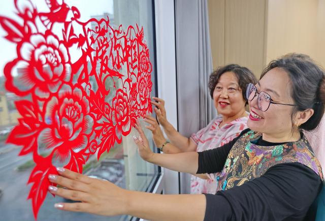 (260929) -- BEIJING, Sept. 29, 2026 (Xinhua) -- Women smooth traditional Chinese paper-cut decorations onto a glass window during an activity celebrating the upcoming National Day in Haigang District of Qinhuangdao, north China's Hebei Province, Sept. 29, 2026. Various events are held across China in celebration of the upcoming National Day. (Photo by Cao Jianxiong/Xinhua)