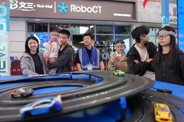 (261001) -- HANGZHOU, Oct. 1, 2026 (Xinhua) -- People experience brain-controlled car racing activities at a digital lifestyle block in Hangzhou, east China's Zhejiang Province, Oct. 1, 2026. A series of activities featuring human-robot interaction is held here from Oct. 1 to 3. (Xinhua/Huang Zongzhi)
