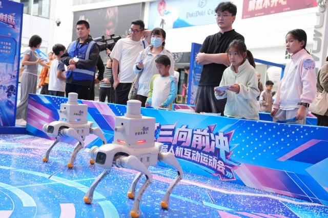 (261001) -- HANGZHOU, Oct. 1, 2026 (Xinhua) -- People experience robot dog shooting activities at a digital lifestyle block in Hangzhou, east China's Zhejiang Province, Oct. 1, 2026. A series of activities featuring human-robot interaction is held here from Oct. 1 to 3. (Xinhua/Huang Zongzhi)