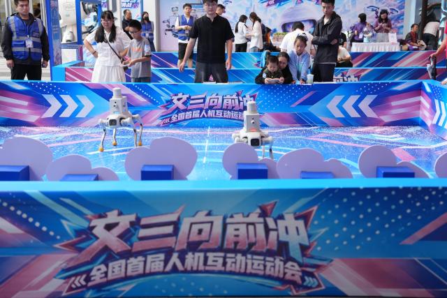 (261001) -- HANGZHOU, Oct. 1, 2026 (Xinhua) -- People experience robot dog shooting activities at a digital lifestyle block in Hangzhou, east China's Zhejiang Province, Oct. 1, 2026. A series of activities featuring human-robot interaction is held here from Oct. 1 to 3. (Xinhua/Huang Zongzhi)