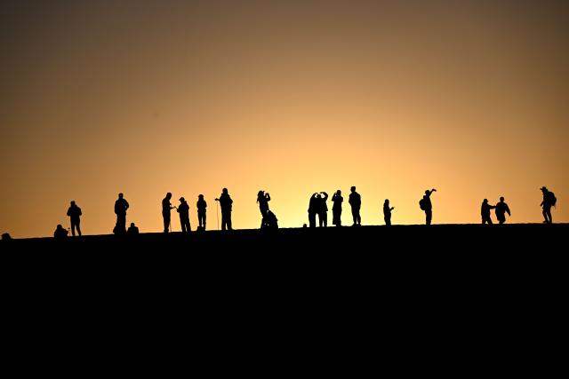 (261001) -- BEIJING, Oct. 1, 2026 (Xinhua) -- Tourists watch the sunrise at the Mingsha Mountain and Crescent Spring Scenic Area in Dunhuang, northwest China's Gansu Province, Oct. 1, 2026. People across China stepped out to fully enjoy their leisure time during the National Day holiday. (Photo by Zhang Xiaoliang/Xinhua)