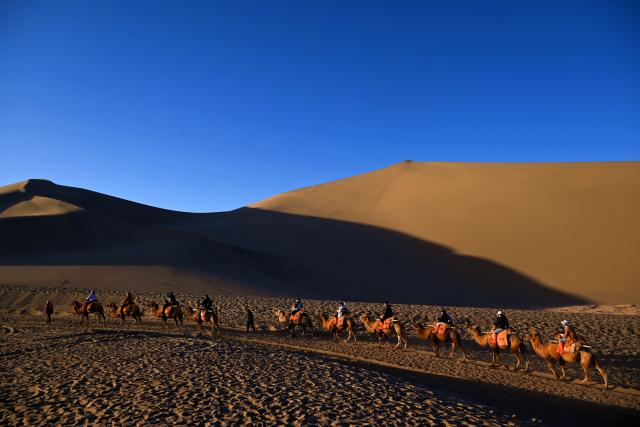 (261001) -- BEIJING, Oct. 1, 2026 (Xinhua) -- Tourists ride camels at the Mingsha Mountain and Crescent Spring Scenic Area in Dunhuang, northwest China's Gansu Province, Oct. 1, 2026. People across China stepped out to fully enjoy their leisure time during the National Day holiday. (Photo by Zhang Xiaoliang/Xinhua)
