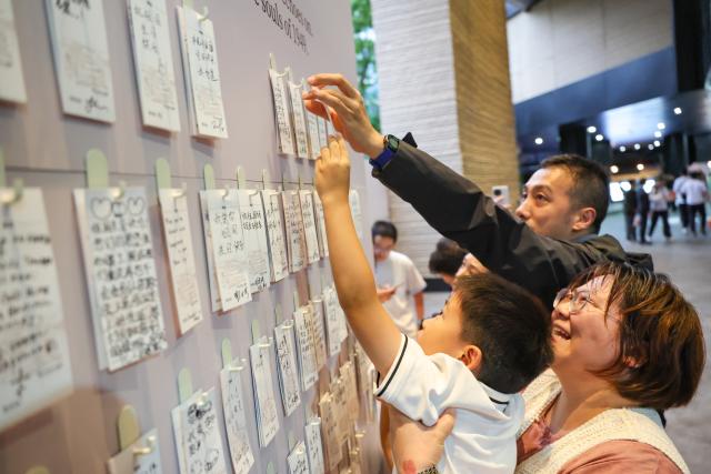 (261001) -- CHONGQING, Oct. 1, 2026 (Xinhua) -- People place their blessings on a wish wall while watching a stage show "Chongqing 1949" in southwest China's Chongqing on Oct. 1, 2026. People across China stepped out to fully enjoy their leisure time during the National Day holiday. (Xinhua/Huang Wei)