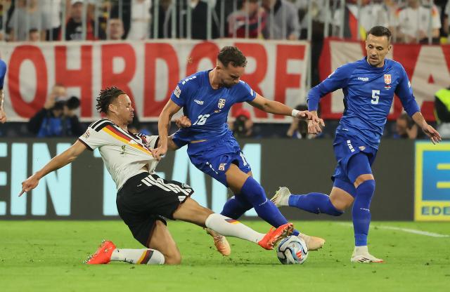 (261002) -- MUNICH, Oct. 2, 2026 (Xinhua) -- Derry Scherhant (L) of Germany vies with Strahinja Erakovic (C) of Serbia during the UEFA Nations League 2026/27 League A Group A2 match between Germany and Serbia in Munich, Germany, Oct. 1, 2026. (Photo by Philippe Ruiz/Xinhua)