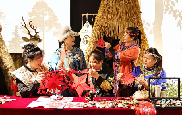 (261002) -- BEIJING, Oct. 2, 2026 (Xinhua) -- Women of Hezhe ethnic group display paper-cutting artworks at a digital experiencing center for intangible cultural heritages in Tongjiang City, northeast China's Heilongjiang Province, Oct. 2, 2026. During the National Day holiday, various cultural and tourism events are held across the country to attract visitors. (Photo by Liu Wanping/Xinhua)