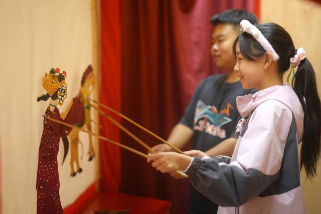 (261002) -- BEIJING, Oct. 2, 2026 (Xinhua) -- Children experience shadow puppet performing at an intangible cultural heritage exhibition hall in Badong County, central China's Hubei Province, Oct. 2, 2026. During the National Day holiday, various cultural and tourism events are held across the country to attract visitors. (Photo by Jiao Guobin/Xinhua)