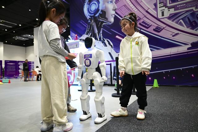 (261005) -- BEIJING, Oct. 5, 2026 (Xinhua) -- Children interact with a robot in a public venue in Hefei, east China's Anhui Province, Oct. 3, 2026. During the National Day holiday, embodied AI robots of various functions rolled out in commercial and cultural blocks have been a major attraction for tourists. Through smart interactions, they have diversified tourism offerings and experiences. (Xinhua/Zhou Mu)