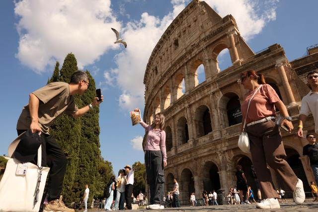 (261006) -- BEIJING, Oct. 6, 2026 (Xinhua) -- A Chinese tourist poses with a Chinese high school textbook with cover of the Colosseum in front of the Colosseum in Rome, Italy, Oct. 4, 2026. (Xinhua/Li Jing)
