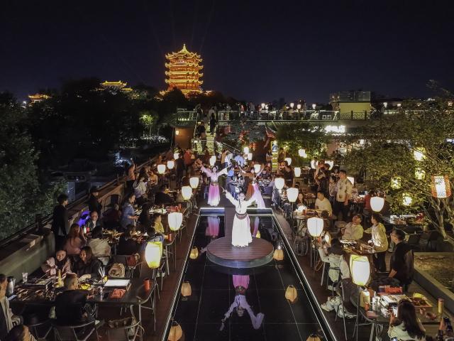 (261006) -- BEIJING, Oct. 6, 2026 (Xinhua) -- A drone photo taken on Oct. 5, 2026 shows people watching a performance with the Yellow Crane Tower in the background in Wuhan, central China's Hubei Province. During the National Day holiday, night tours were launched across China to create diversified consumption scenes. (Photo by Zhao Jun/Xinhua)
