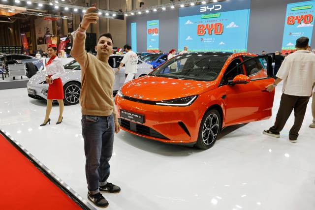 (261006) -- BUCHAREST, Oct. 6, 2026 (Xinhua) -- A visitor poses for photo before a car model produced by Chinese producer BYD during the first day of Bucharest Auto Show & Accessories in Bucharest, Romania, Oct. 6, 2026. (Photo by Cristian Cristel/Xinhua)