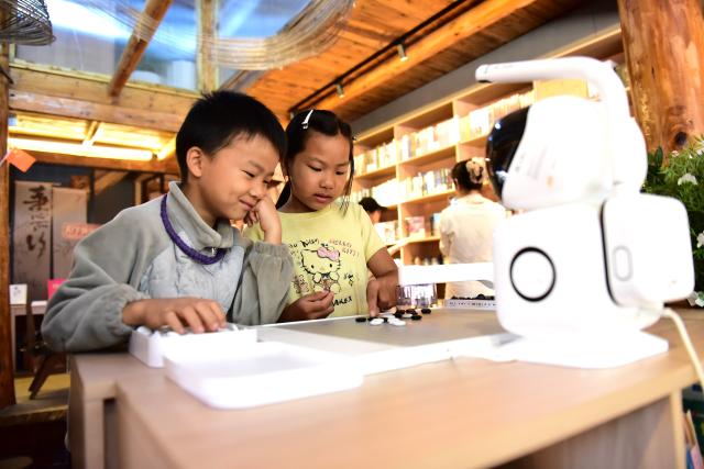 (261007) -- BEIJING, Oct. 7, 2026 (Xinhua) -- Children play a board game with an AI robot at Basha Village in Congjiang County, southwest China's Guizhou Province, Oct. 6, 2026. Advanced technologies such as exoskeleton devices, AI-powered glasses and robots have enabled diverse and dazzling experiences at tourist destinations across China during the National Day holiday. (Photo by Shi Honghui/Xinhua)