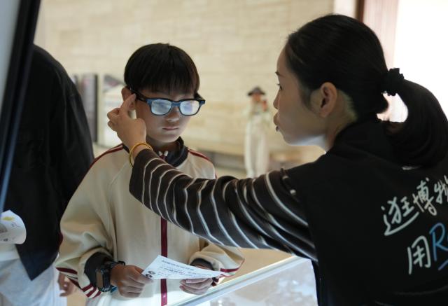 (261007) -- BEIJING, Oct. 7, 2026 (Xinhua) -- A staff member introduces AI glasses to a tourist at the Liangzhu Museum in Hangzhou, east China's Zhejiang Province, Oct. 6, 2026. Advanced technologies such as exoskeleton devices, AI-powered glasses and robots have enabled diverse and dazzling experiences at tourist destinations across China during the National Day holiday. (Xinhua/Han Chuanhao)