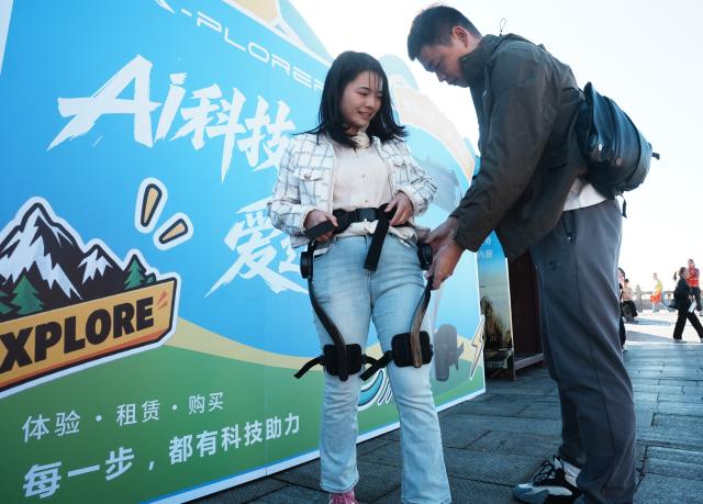 (261007) -- BEIJING, Oct. 7, 2026 (Xinhua) -- A staff member helps a tourist put on an exoskeleton robot at the Hengshan Mountain scenic area in Hengyang City, central China's Hunan Province, Oct. 6, 2026. Advanced technologies such as exoskeleton devices, AI-powered glasses and robots have enabled diverse and dazzling experiences at tourist destinations across China during the National Day holiday. (Photo by Cao Zhengping/Xinhua)