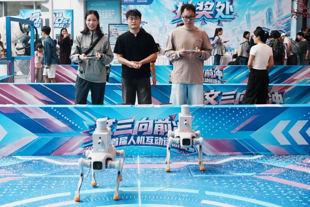 (261007) -- BEIJING, Oct. 7, 2026 (Xinhua) -- Tourists play a shooting game by manipulating robotic dogs at a block for digital lifestyle in Hangzhou, east China's Zhejiang Province, Oct. 1, 2026. Advanced technologies such as exoskeleton devices, AI-powered glasses and robots have enabled diverse and dazzling experiences at tourist destinations across China during the National Day holiday. (Photo by Long Wei/Xinhua)