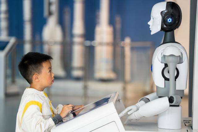 (261007) -- BEIJING, Oct. 7, 2026 (Xinhua) -- A child interacts with a robot at a science and technology museum in Bijie, southwest China's Guizhou Province, Oct. 6, 2026. Advanced technologies such as exoskeleton devices, AI-powered glasses and robots have enabled diverse and dazzling experiences at tourist destinations across China during the National Day holiday. (Photo by Luo Dafu/Xinhua)