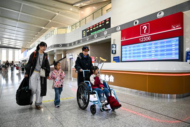 (261007) -- BEIJING, Oct. 7, 2026 (Xinhua) -- A railway staff member (2nd R) helps with a passenger's wheelchair at Hohhot East Railway Station in Hohhot, north China's Inner Mongolia Autonomous Region, Oct. 7, 2026. As the National Day holiday is drawing to a close, return travel flows increase across the country. (Xinhua/Li Zhipeng)