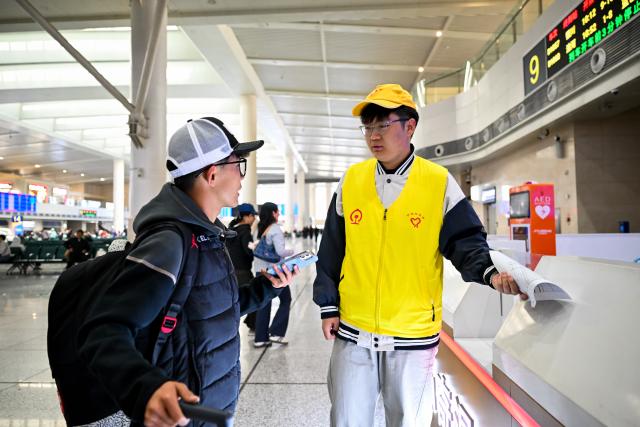 (261007) -- BEIJING, Oct. 7, 2026 (Xinhua) -- A volunteer (R) helps a passenger at Hohhot East Railway Station in Hohhot, north China's Inner Mongolia Autonomous Region, Oct. 7, 2026. As the National Day holiday is drawing to a close, return travel flows increase across the country. (Xinhua/Li Zhipeng)