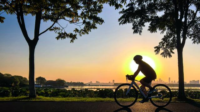 (261008) -- WUHAN, Oct. 8, 2026 (Xinhua) -- This photo taken with a mobile phone on Oct. 7, 2026 shows a tourist riding a bicycle by the East Lake at sunset in Wuhan, central China's Hubei Province. (Xinhua/Shen Hongbing)
