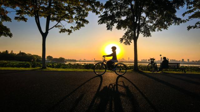 (261008) -- WUHAN, Oct. 8, 2026 (Xinhua) -- This photo taken with a mobile phone on Oct. 7, 2026 shows a tourist riding a bicycle by the East Lake at sunset in Wuhan, central China's Hubei Province. (Xinhua/Shen Hongbing)