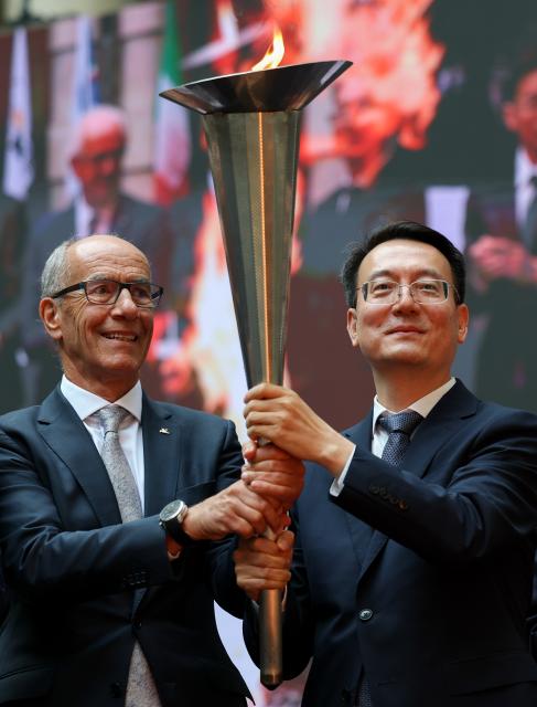 (261009) -- TURIN, Oct. 9, 2026 (Xinhua) -- Mayor of Changchun Gu Gang (R) and president of FISU Leonz Eder hold the torch from the first World University Games held in Turin in 1959 during the flame collection ceremony for the Changchun 2027 Winter Universiade in Turin, Italy, Oct. 8, 2026. (Xinhua/Wang Kaiyan)