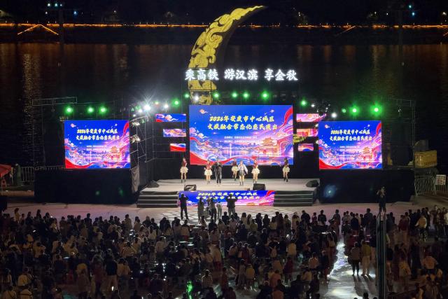 (261009) -- ANKANG, Oct. 9, 2026 (Xinhua) -- Tourists watch a welfare performance on the bank of the Hanjiang River in Ankang, northwest China's Shaanxi Province, Oct. 7, 2026.
  The city of Ankang receives a surging number of tourists, thanks to the Xi'an-Ankang high-speed railway officially put into operation on Sept. 28 this year. The travel time between Xi'an, capital of Shaanxi, and Ankang has been slashed to less than one hour. (Photo by Liu Yang/Xinhua)