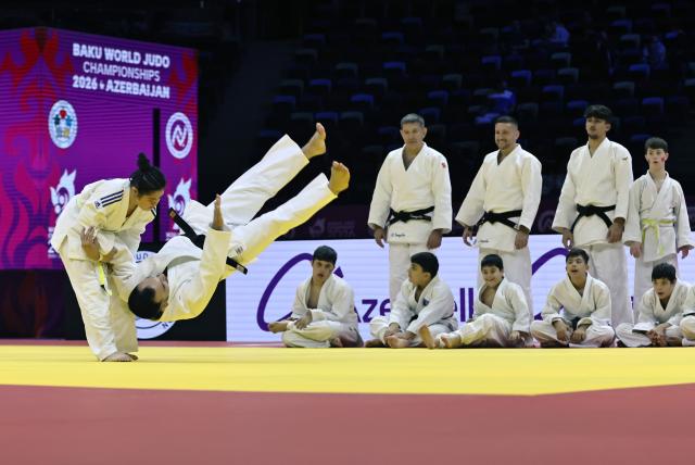 (261010) -- BAKU, Oct. 10, 2026 (Xinhua) -- A girl practices judo as others watch on the official competition mat after the preliminary matches of the 2026 World Senior Judo Championships in Baku, Azerbaijan, Oct. 9, 2026. Azerbaijani judo coaches guide children with Down syndrome to experience judo. Under the supervision of elite athletes and coaches, the children learn basic techniques and judo etiquette on an official competition mat, embodying inclusive sport and judo's educational mission. (Xinhua/Chen Junfeng)