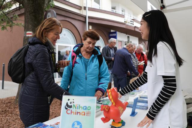 (261010) -- SIOFOK, Oct. 10, 2026 (Xinhua) -- A staff member introduces Chinese tourism to visitors during the 2026 Siofok Fish Festival in Siofok, Hungary, Oct. 10, 2026. Sit on the southern shore of Lake Balaton, Hungary's largest lake, Siofok is one of the country's leading lakeside holiday destinations. The city's annual fish festival is a major autumn event, with its 13th edition taking place on Oct. 9-11, 2026. (Xinhua/Hu Zhixuan)