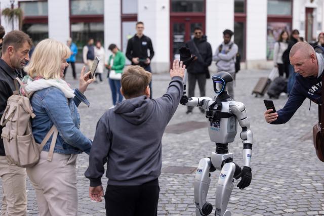 (261011) -- LJUBLJANA, Oct. 11, 2026 (Xinhua) -- A visitor gives a high-five to the Unitree G1 humanoid robot conductor before the parade of the Ljubljana Wind Orchestra in Ljubljana, Slovenia, Oct. 11, 2026. (Photo by Zeljko Stevanic/Xinhua)
