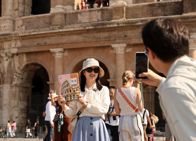 (261012) -- WARSAW, Oct. 12, 2026 (Xinhua) -- A Chinese tourist, holding a Chinese high school textbook with the Colosseum on the cover, poses for photo in front of the Colosseum in Rome, Italy, Oct. 4, 2026. (Xinhua/Li Jing)