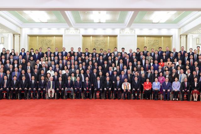 (261012) -- BEIJING, Oct. 12, 2026 (Xinhua) -- Wang Huning, a member of the Standing Committee of the Political Bureau of the Communist Party of China (CPC) Central Committee and chairman of the National Committee of the Chinese People's Political Consultative Conference (CPPCC), meets and poses for a group photo with representatives attending a conference marking the 70th anniversary of the establishment of the All-China Federation of Returned Overseas Chinese (ACFROC) in Beijing, capital of China, Oct. 12, 2026. Wang attended the conference and delivered a speech. (Xinhua/Liu Bin)