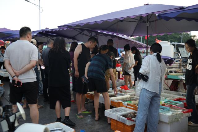 (261013) -- HAIKOU, Oct. 13, 2026 (Xinhua) -- Tourists buy seafood at a seafood market along Fugang Road in Tanmen Town of Qionghai, south China's Hainan Province, Oct. 2, 2026. TO GO WITH "Across China: Fishing tourism on the rise in historic south China port" (Xinhua)