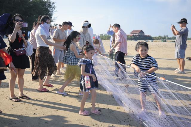 (261013) -- HAIKOU, Oct. 13, 2026 (Xinhua) -- Tourists experience traditional seine fishing on the beach in Tanmen Town of Qionghai, south China's Hainan Province, Oct. 2, 2026. TO GO WITH "Across China: Fishing tourism on the rise in historic south China port" (Xinhua)