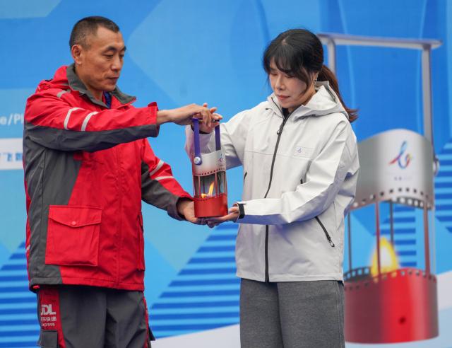 (261014) -- CHANGCHUN, Oct. 14, 2026 (Xinhua) -- Yang Zhanshan (L), a delivery worker, passes the flame latern to Zhou Yang, Chinese Olympic champion in short track speed skating, during a flame welcome ceremony of Changchun 2027 Winter Universiade in Changchun, northeast China's Jilin Province, Oct. 14, 2026. (Xinhua/Yan Linyun)