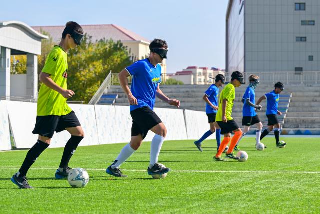 (261015) -- URUMQI, Oct. 15, 2026 (Xinhua) -- Players train at Xinjiang Special Education Vocational Secondary School in Changji Hui Autonomous Prefecture, northwest China's Xinjiang Uygur Autonomous Region, Oct. 14, 2026. Xinjiang's first blind football team is known as the 'Wei Wei Wei' team. It takes its name from the call players shout to locate teammates and avoid collisions. This call is the communication code of this special sport.
In blind football, players wear light-blocking blindfolds throughout the match. They track the ball by the bell inside it and keep calling 'wei, wei, wei' to gauge teammates' positions, enabling them to dribble, pass and shoot without sight. In training, they run, collide, feel the boundary boards, and build muscle memory through countless falls and getting back up. For visually impaired teenagers who rarely dare to sprint at full speed in daily life, this enclosed pitch is a place where they can run freely.
'We cannot see the world, but we strive to make the world see us.' In the darkness, guided by their calls and the sound of the ball, these young athletes break through barriers and shine brightly on the green pitch. (Xinhua/Ding Lei)