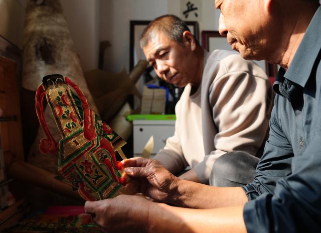 (261015) -- SHENYANG, Oct. 15, 2026 (Xinhua) -- Xu Zilin (R) discusses with his brother on the making of shadow puppets in Lingyuan City, northeast China's Liaoning Province, Oct. 10, 2026.
  Lingyuan shadow puppetry, a national-level intangible cultural heritage in China, comes vividly alive amid dazzling light and shadow. Movements of the puppets embody the local folk traditions, which have been passed down through generations.
  Xu Zilin was born in 1964 to a family that has the Lingyuan shadow puppetry as its walk of life for ages. More than 40 years of professional experience made Xu a representative inheritor of the craft and an influential figure in the trade. Many of his vocal passages have been modeled for teaching.
  To better promote shadow plays, Xu founded a shadow puppetry troupe and brought quality productions to the grassroots level. Over the years, Xu and his troupe have performed more than 4,000 shows in Liaoning and neighboring provinces. (Xinhua/Li Gang)