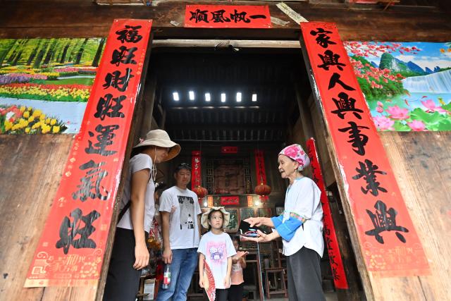 (261016) -- LONGSHENG, Oct. 16, 2026 (Xinhua) -- Hou Yujin (R) introduces the embroidery pattern to tourists at her stilted house in Longji Village of Longsheng County, south China's Guangxi Zhuang Autonomous Region, Oct. 15, 2026. Longji Village, home mainly to the Zhuang ethnic group, features traditional wooden houses nestled among terraced fields and retains its distinctive ethnic cultural heritage.
   Hou Yujin, an elderly local woman who lives in one of the century-old stilted buildings of Zhuang ethnic group in the village, has volunteered to offer free guided tours to tourists. Despite never having attended a single day of school, Hou taught herself Mandarin through great efforts to share with visitors the history of her house and the dramatic changes of the village. (Xinhua/Lu Boan)
