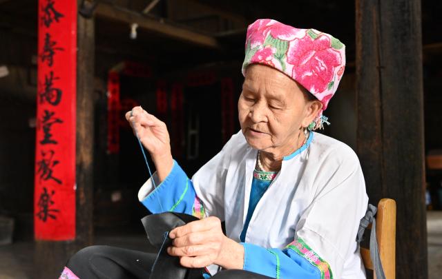 (261016) -- LONGSHENG, Oct. 16, 2026 (Xinhua) -- Hou Yujin makes an embroidery work in Longji Village of Longsheng County, south China's Guangxi Zhuang Autonomous Region, Oct. 15, 2026. Longji Village, home mainly to the Zhuang ethnic group, features traditional wooden houses nestled among terraced fields and retains its distinctive ethnic cultural heritage.
   Hou Yujin, an elderly local woman who lives in one of the century-old stilted buildings of Zhuang ethnic group in the village, has volunteered to offer free guided tours to tourists. Despite never having attended a single day of school, Hou taught herself Mandarin through great efforts to share with visitors the history of her house and the dramatic changes of the village. (Xinhua/Lu Boan)