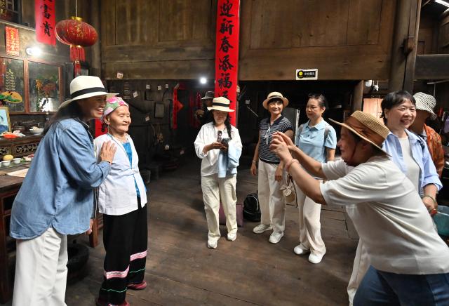 (261016) -- LONGSHENG, Oct. 16, 2026 (Xinhua) -- A tourist poses for photos with Hou Yujin (2nd L) in Longji Village of Longsheng County, south China's Guangxi Zhuang Autonomous Region, Oct. 15, 2026. Longji Village, home mainly to the Zhuang ethnic group, features traditional wooden houses nestled among terraced fields and retains its distinctive ethnic cultural heritage.
   Hou Yujin, an elderly local woman who lives in one of the century-old stilted buildings of Zhuang ethnic group in the village, has volunteered to offer free guided tours to tourists. Despite never having attended a single day of school, Hou taught herself Mandarin through great efforts to share with visitors the history of her house and the dramatic changes of the village. (Xinhua/Lu Boan)