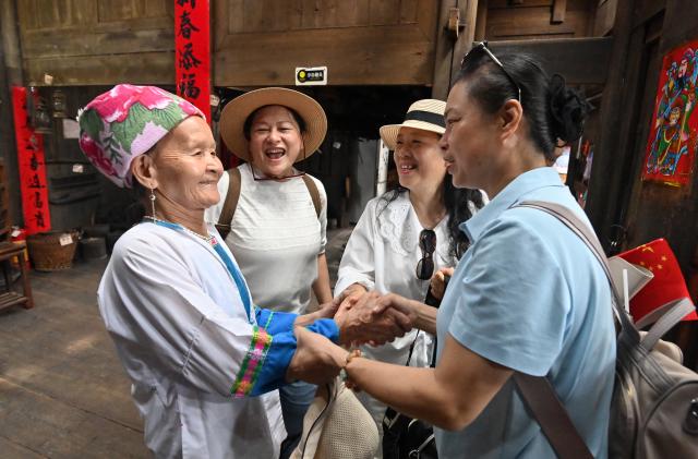 (261016) -- LONGSHENG, Oct. 16, 2026 (Xinhua) -- Tourists bid farewell to Hou Yujin (L, front) in Longji Village of Longsheng County, south China's Guangxi Zhuang Autonomous Region, Oct. 15, 2026. Longji Village, home mainly to the Zhuang ethnic group, features traditional wooden houses nestled among terraced fields and retains its distinctive ethnic cultural heritage.
   Hou Yujin, an elderly local woman who lives in one of the century-old stilted buildings of Zhuang ethnic group in the village, has volunteered to offer free guided tours to tourists. Despite never having attended a single day of school, Hou taught herself Mandarin through great efforts to share with visitors the history of her house and the dramatic changes of the village. (Xinhua/Lu Boan)