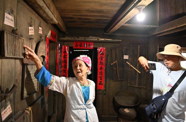 (261016) -- LONGSHENG, Oct. 16, 2026 (Xinhua) -- Hou Yujin (L) gives an introduction to a tourist at her stilted house in Longji Village of Longsheng County, south China's Guangxi Zhuang Autonomous Region, Oct. 15, 2026. Longji Village, home mainly to the Zhuang ethnic group, features traditional wooden houses nestled among terraced fields and retains its distinctive ethnic cultural heritage.
   Hou Yujin, an elderly local woman who lives in one of the century-old stilted buildings of Zhuang ethnic group in the village, has volunteered to offer free guided tours to tourists. Despite never having attended a single day of school, Hou taught herself Mandarin through great efforts to share with visitors the history of her house and the dramatic changes of the village. (Xinhua/Lu Boan)