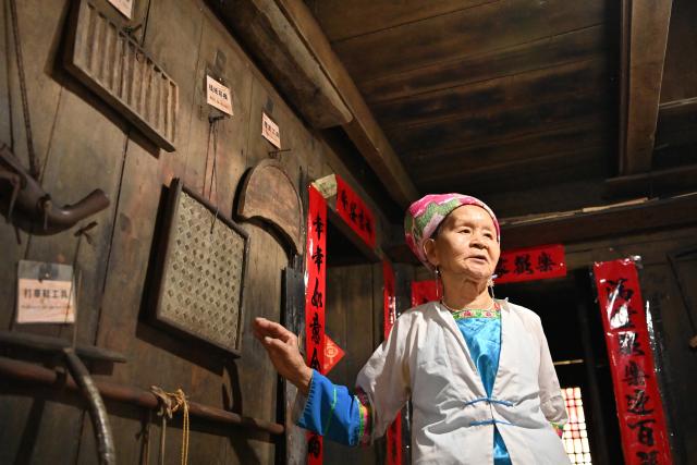 (261016) -- LONGSHENG, Oct. 16, 2026 (Xinhua) -- Hou Yujin gives an introduction to tourists at her stilted house in Longji Village of Longsheng County, south China's Guangxi Zhuang Autonomous Region, Oct. 15, 2026. Longji Village, home mainly to the Zhuang ethnic group, features traditional wooden houses nestled among terraced fields and retains its distinctive ethnic cultural heritage.
   Hou Yujin, an elderly local woman who lives in one of the century-old stilted buildings of Zhuang ethnic group in the village, has volunteered to offer free guided tours to tourists. Despite never having attended a single day of school, Hou taught herself Mandarin through great efforts to share with visitors the history of her house and the dramatic changes of the village. (Xinhua/Lu Boan)