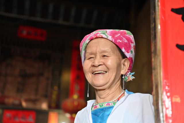(261016) -- LONGSHENG, Oct. 16, 2026 (Xinhua) -- Hou Yujin is pictured at her stilted house in Longji Village of Longsheng County, south China's Guangxi Zhuang Autonomous Region, Oct. 15, 2026. Longji Village, home mainly to the Zhuang ethnic group, features traditional wooden houses nestled among terraced fields and retains its distinctive ethnic cultural heritage.
   Hou Yujin, an elderly local woman who lives in one of the century-old stilted buildings of Zhuang ethnic group in the village, has volunteered to offer free guided tours to tourists. Despite never having attended a single day of school, Hou taught herself Mandarin through great efforts to share with visitors the history of her house and the dramatic changes of the village. (Xinhua/Lu Boan)