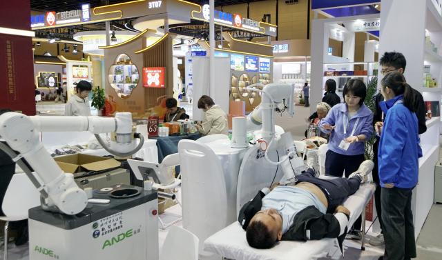 (261016) -- BEIJING, Oct. 16, 2026 (Xinhua) -- A visitor tries massage therapy by a smart robot during the Beijing International Traditional Healthcare Exhibition in Beijing, capital of China, Oct. 16, 2026. The event was kicked off here on Friday. (Photo by Bi Shanghong/Xinhua)