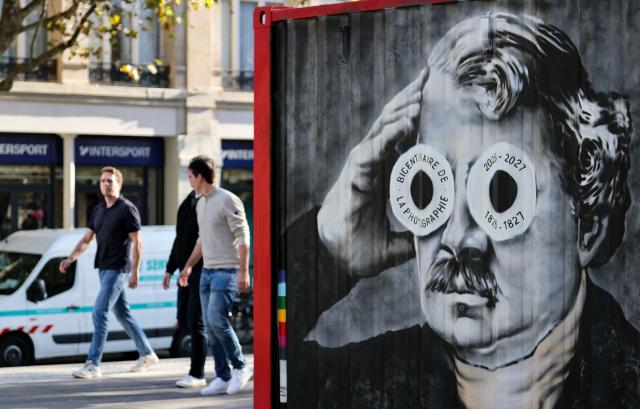 (261016) -- PARIS, Oct. 16, 2026 (Xinhua) -- People walk past a street art installation commemorating Louis Daguerre at Place de la Republique in Paris, France, Oct. 16, 2026. A bronze plaque titled "An Unexpected Detail" was unveiled at Place de la Republique in Paris on Thursday. It honors "Boulevard du Temple," an image taken in 1838 by French photography pioneer Louis Daguerre and believed to be the first photograph to show people. (Xinhua/Wu Huiwo)