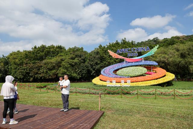 (261017) -- SHENZHEN, Oct. 17, 2026 (Xinhua) -- People pose for photos with a flower decoration themed on the 2026 APEC "China Year," in Shenzhen, south China's Guangdong Province, Oct. 17, 2026. The APEC Economic Leaders' Meeting will be held in Shenzhen next month. (Xinhua/Liang Xu)