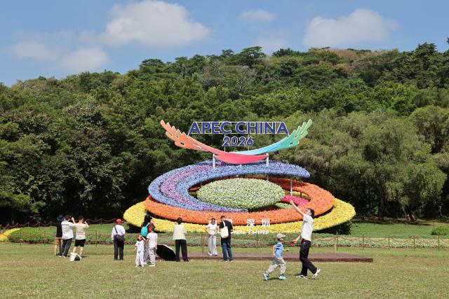 (261017) -- SHENZHEN, Oct. 17, 2026 (Xinhua) -- People pose for photos with a flower decoration themed on the 2026 APEC "China Year," in Shenzhen, south China's Guangdong Province, Oct. 17, 2026. The APEC Economic Leaders' Meeting will be held in Shenzhen next month. (Xinhua/Liang Xu)
