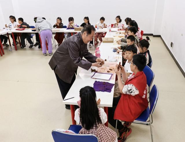 (261017) -- SHENYANG, Oct. 17, 2026 (Xinhua) -- Sun Yu'en guides children in making Chaoyang red clay figure works at a library in Chaoyang, northeast China's Liaoning Province, April 30, 2026. Chaoyang red clay figure is a provincial-level intangible cultural heritage in Liaoning Province, northeast China. 
  Sun Yu'en, an inheritor of this craft, has loved the art since childhood. In 1998, he devoted himself to the craft and learned the core skills from his teacher. Sun's artworks emphasize the expressions and details of the figures, embodying rustic charm. He has also created a series of moving clay figures, which are popular among young people. (Xinhua)