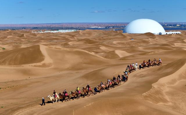 (261017) -- ZHONGWEI, Oct. 17, 2026 (Xinhua) -- An aerial drone photo taken on Oct. 17, 2026 shows tourists riding camels at the Tengger Desert in Zhongwei, northwest China's Ningxia Hui Autonomous Region. Marking the beginning of a desert self-driving event, a ceremony was held here on Saturday, gathering more than 500 vehicles for self-driving tours and over 1,000 tourists. (Xinhua/Wang Peng)